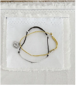 Close-up of minimalist handmade woven rope bracelets with vintage silver charms on white fabric