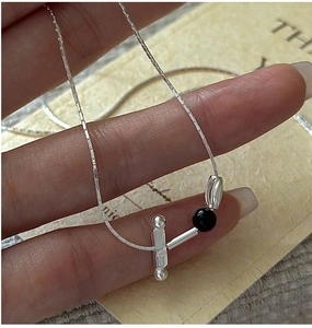 Detail of S925 silver necklace with black bead, metal tube, and horizontal bar pendant