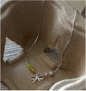 Detailed shot of S925 silver bow necklace with colorful beads on a natural textured surface