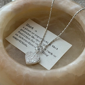 S925 sterling silver heart necklace with filigree texture on a stone pedestal