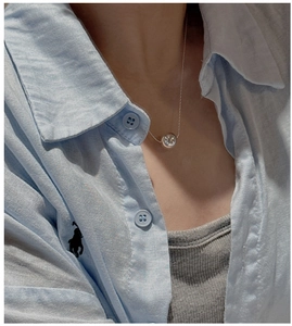 Detail of a minimalist silver bead pendant necklace worn over a casual blue shirt