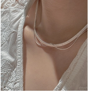Detail of layered S925 silver choker and thin chain necklace on white lace shirt