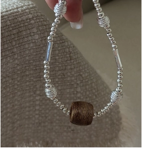 Detail of silver beaded bracelet with a vintage brown wooden barrel bead in a close-up view