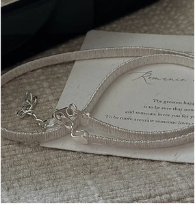 Macro detail of silver woven chain necklace with a heart-shaped clasp and extender