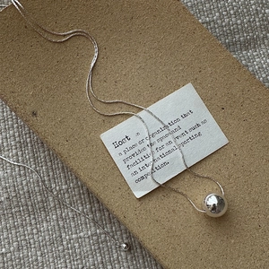 Minimalist S925 sterling silver long ball pendant necklace on a textured background