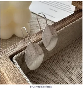 Detail of leaf-shaped silver drop earrings with brushed texture on a wooden edge