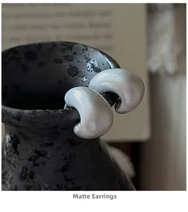 Detailed close-up of matte silver vintage earrings resting on a textured black vase