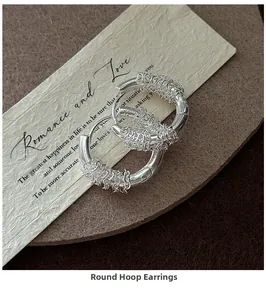 Detail of S925 sterling silver woven hoop earrings on textured beige paper