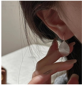 Detail of S925 sterling silver leaf earrings with brushed metal texture on a model