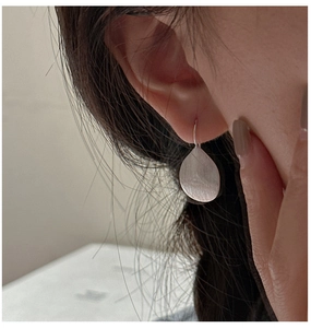 Close-up of teardrop silver earrings with brushed metal texture worn by a model