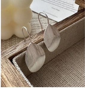 Macro shot of silver brushed leaf earrings showing matte texture and long ear hooks