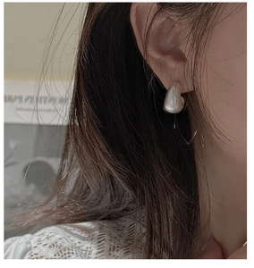 Close-up of minimalist heart-shaped white pearl stud earring worn on model ear