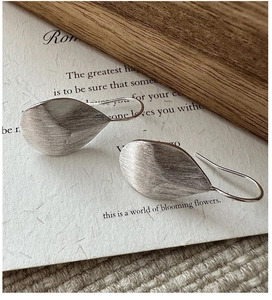 Detailed macro view of S925 sterling silver brushed leaf earrings on artistic paper