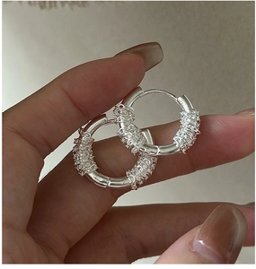 Detailed view of S925 sterling silver woven hoop earrings held by a model for scale