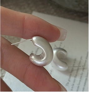 Macro detail of silver matte textured hollow C-shaped stud earrings in a modern design