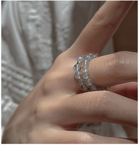 Detail of double-layer beaded ring with grey moonstone and gold accent on a finger