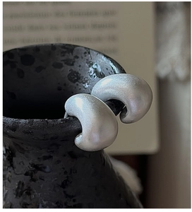 Macro detail of matte S925 silver C-shape earrings resting on a black ceramic vase