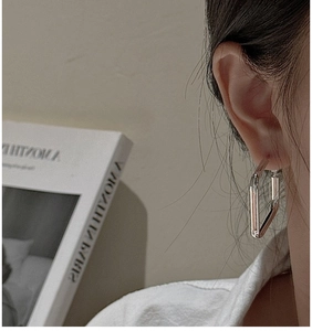Close-up of minimalist silver rectangular hoop earrings worn by a model in Paris style