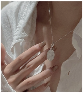 Detail of silver daisy oval pendant with hammered texture worn on a white shirt