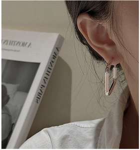 Detail view of a minimalist silver S925 geometric earring on a model with an artistic book