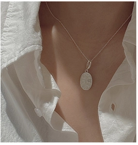 Detail of S925 sterling silver oval pendant with delicate floral engraving on a fine chain
