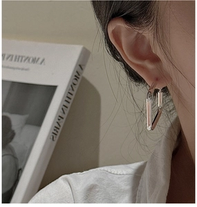 Macro side view of silver geometric triangular earrings worn by a model in a minimalist setting