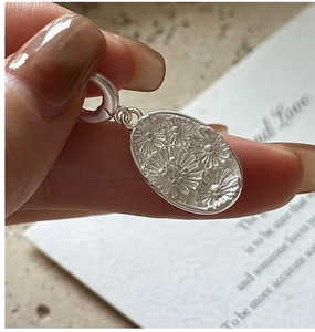 Detailed close-up of oval silver pendant with intricate daisy flower relief and lobster clasp