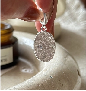 Macro detail of S925 sterling silver daisy pendant with central zircon on female hand