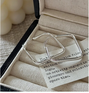 Detail shot of square S925 sterling silver hoop earrings on beige jewelry lining