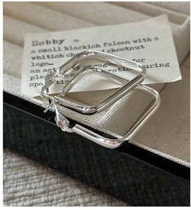 Macro detail of polished silver square hoop earrings displayed on beige fabric box