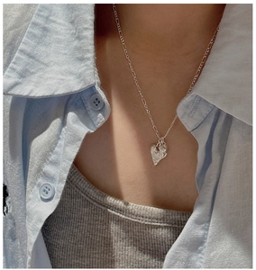 Detail of silver heart necklace with irregular texture on a model wearing a blue shirt