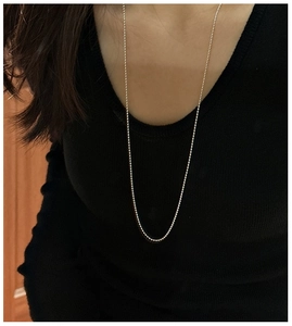 Detail of a long minimalist silver ball chain necklace worn over a black sweater
