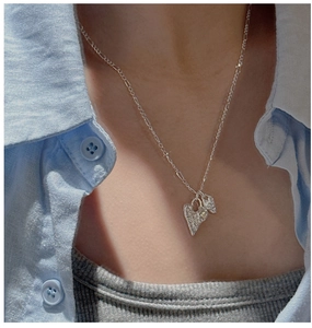 Detail of heart pendant necklace with hammered texture on a Figaro chain with model