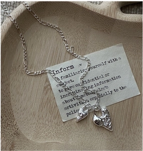 Macro shot of silver textured double heart pendant on a figaro chain in a wooden tray
