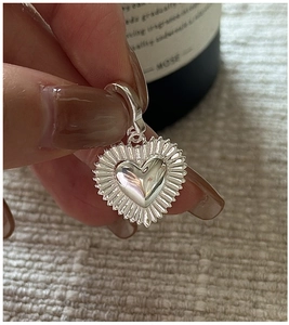 Close-up of S925 silver heart pendant with radiant texture held by hand for detail