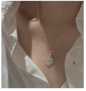 Macro detail of a vintage S925 silver heart pendant necklace on a white shirt