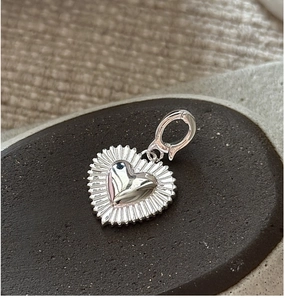 Macro shot of silver heart pendant with pleated edges on a gray stone base