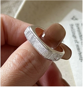 Macro shot of silver ring with brushed metal texture and a small embedded diamond