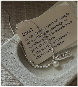 Detailed view of S925 silver necklace with white pearl on a stone textured surface
