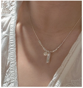 Close-up of S925 silver necklace with textured bar and round pendant on a model