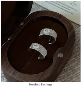Macro shot of silver brushed metal earrings with floral relief on a wooden jewelry box