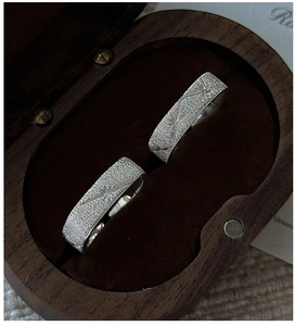 Macro detail of silver rings with brushed finish and dragonfly engraving in a wood box