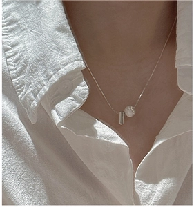 Close-up of a brushed silver ball necklace worn with a white minimalist shirt