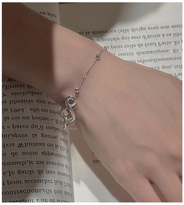 Detail of S925 sterling silver infinity bracelet worn on wrist against book pages