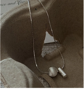 Detail of S925 silver necklace featuring a brushed bead and polished cylinder pendant