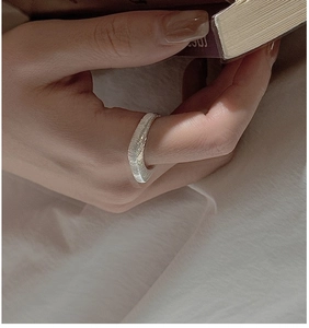 Close-up of a wide silver S925 ring with brushed texture on a model hand with a book