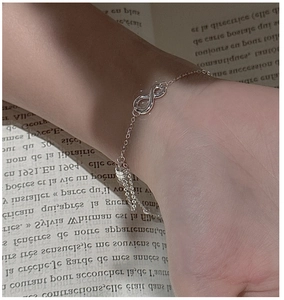 Macro shot of silver infinity bracelet with adjustable slider on a wrist over a book