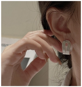 Detail of silver S925 earrings with textured horizontal lines on a model side view