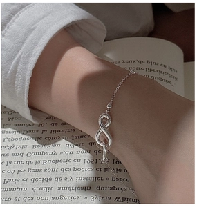 Elegant infinity symbol silver bracelet worn on wrist against a vintage book background