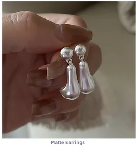 Detailed view of matte silver fluid teardrop earrings held to show modern minimalist texture